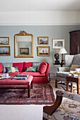 Red sofa below mirror and paintings in gilt frames in living room