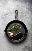 Black cast iron frying pan with oil, garlic, pepper and rosemary