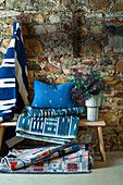 Bank mit Teppich, Kissen und Decke in Blautönen vor Natursteinwand