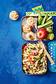 Sushi-Reisbällchen mit Teriyaki-Hähnchen, Gemüse und Obst und Nudelsalat mit Schinken und Mais in Lunchboxen