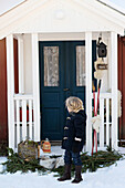 Child standing in front of a house entrance decorated for Christmas