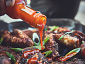 Pouring Sriracha sauce over chicken wings
