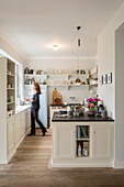View into white fitted kitchen with woman in background