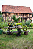 Rustic seating area with table made of old wooden door and sewing machine base, potted hydrangeas, bouquet of spurge and wreath on back of chair