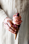 A hand holding cherry ice cream in a cone