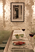 Gedeckter Tisch mit Parmaschinken, Oliven und Rotwein in italienischem Ambiente