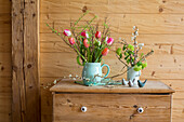Bouquet of tulips and flowering twigs in jug vases on a wooden chest of drawers