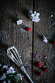 Flowers, raspberries and a whisk on a wooden surface