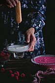 Sponge fingers being dipped in milk with raspberry cream in the foreground