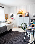 Schlafzimmer mit weißer Holzvertäfelung und verschiedenen Sitzmöglichkeiten