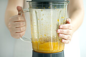 Hands holding blender containing pureed apricots