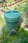 Compost tumbler bin next to vegetable patch in garden