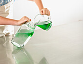 Hands pouring warm green liquid into jar of cold water