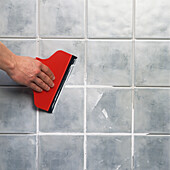 Grout being applied to tiles using a squeegee