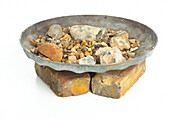 Dustbin lid filled with rocks upended on two bricks