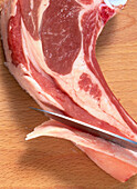 Slicing excess fat from a lamb chop with a chef's knife