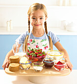 Girl holding the ingredients for strawberry cheesecakes