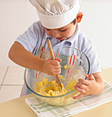 Boy beating together butter, eggs and sugar in mixing bowl