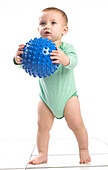 Baby boy standing holding a bumpy ball toy