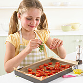 Girl scattering thyme leaves over halved tomatoes