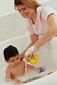Woman pouring water from beaker into bath as baby is bathing