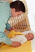 Father wrapping baby girl in warm yellow blanket