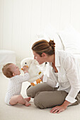 Mother playing with baby boy holding large cuddly toy duck