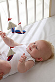 Baby boy lying down reaching up to sailing boat mobile