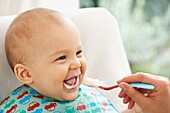 Baby boy laughing while being fed with spoon