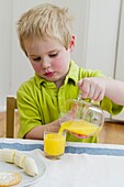 Boy pouring orange juice from jug into glass