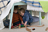 Boys sitting under table playing with toy train set