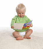 Baby boy sitting with a booklet in his hands