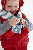 Boy wearing hooded gilet and knitted snake scarf