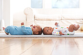 Twin baby boys lying on backs on mat