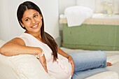 Smiling pregnant woman sitting on chaise longue