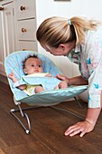 Mother talking to baby girl lying in baby bouncer