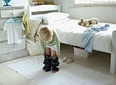 Boy putting on trousers in bedroom