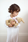 Young girl in pyjama cradling toy rabbit
