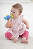 Baby girl sitting on carpet holding toy up to mouth