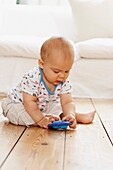 Baby boy sitting on wooden floor playing with rattle toy