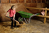 Girl shovelling manure into wheelbarrow