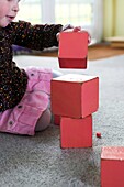 Girl stacking red wooden blocks