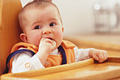 Baby sitting in a highchair eating a biscuit