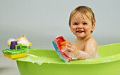 Baby girl in bath playing with plastic toy boats