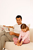 Father reading newspaper while girl uses foot roller