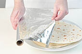 Placing foil over tortillas on a plate