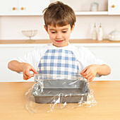 Boy holding cling film over baking tray