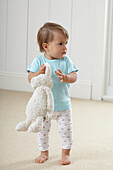 Baby girl standing holding a toy rabbit
