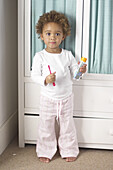 Toddler holding red toothbrush and tube of toothpaste