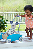 Baby girl pushing cart containing toy rabbit